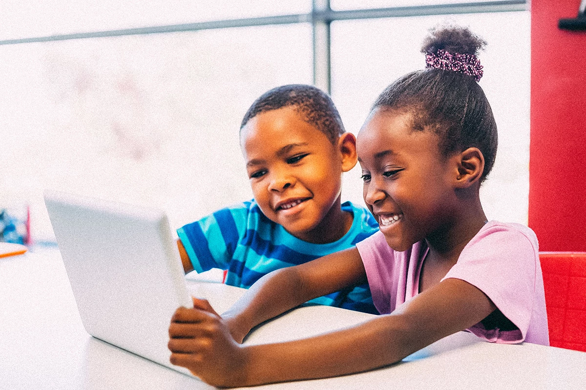 Two young students smiling and working on laptop together. 