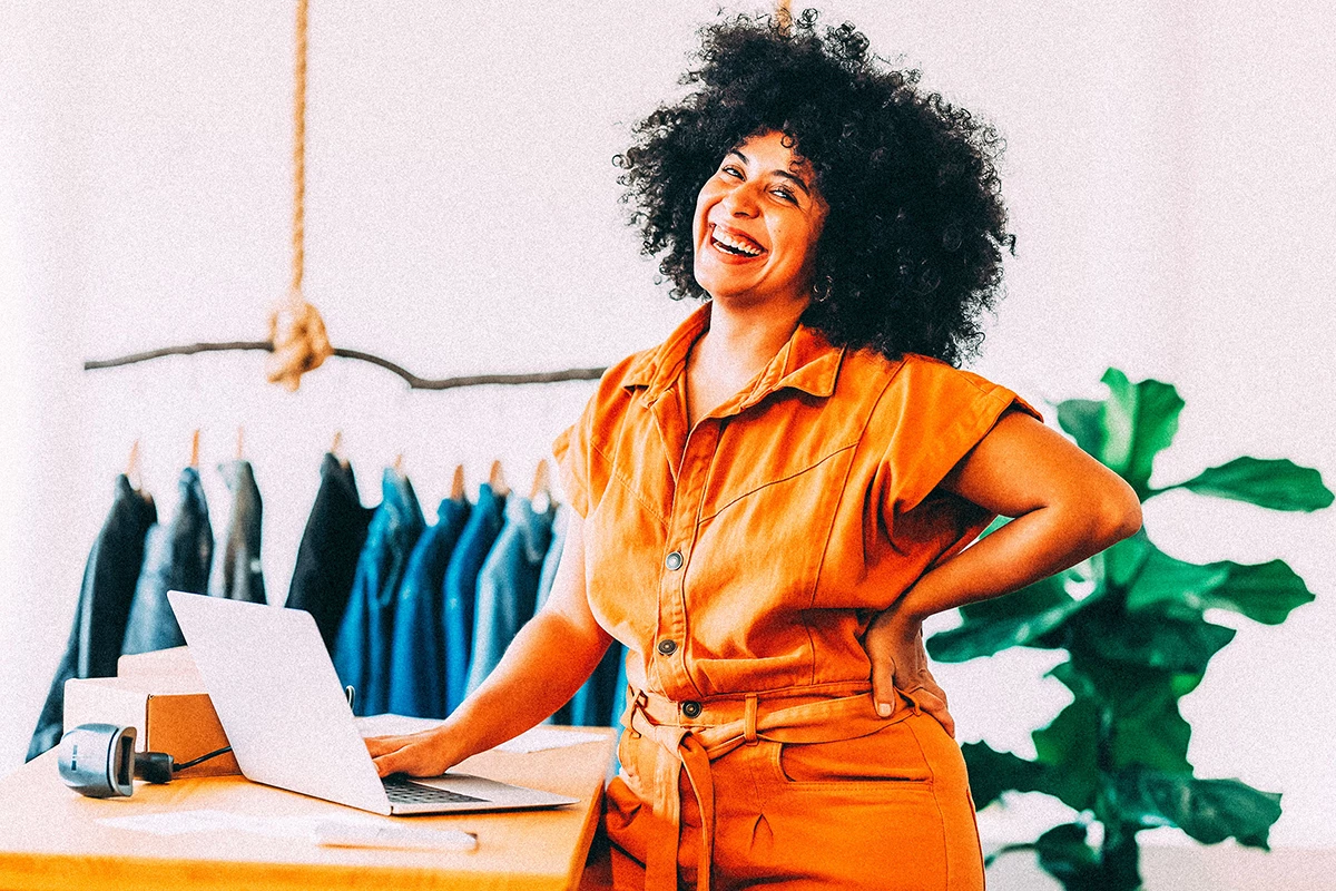 Small business owner smiling in her retail shop while creating videos on her laptop