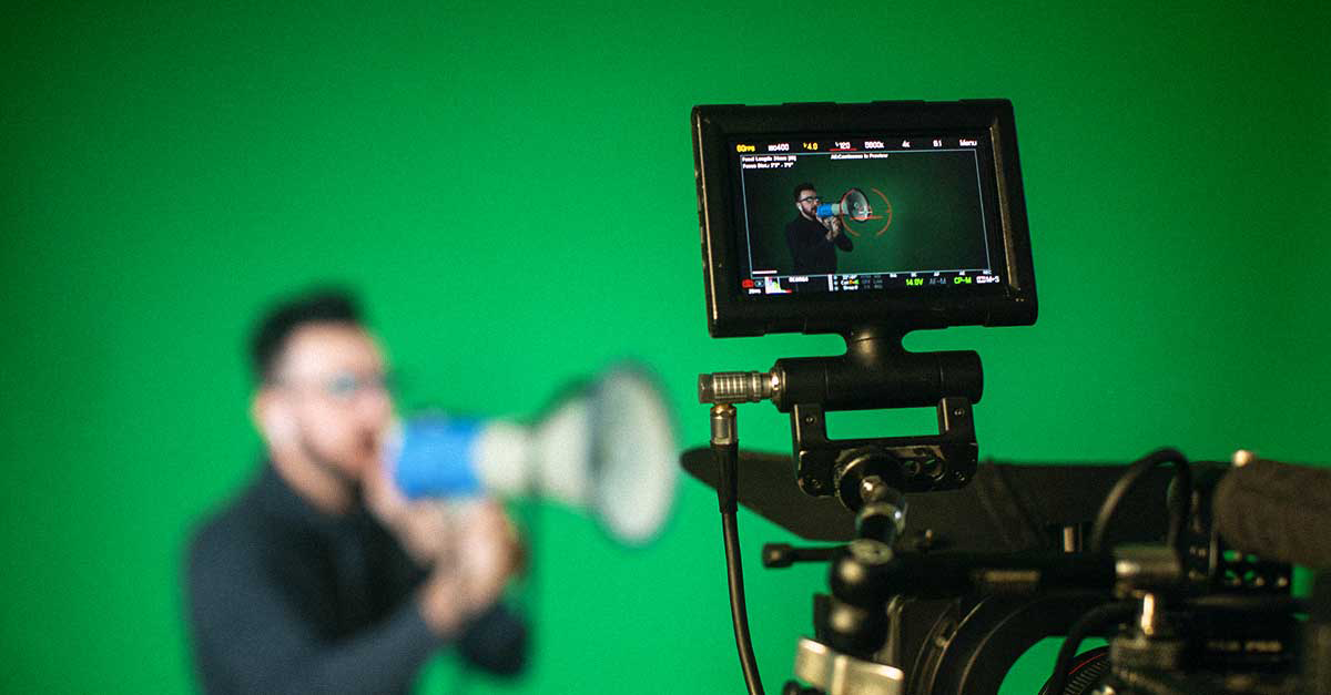 Man with megaphone blurred against a green screen recording.