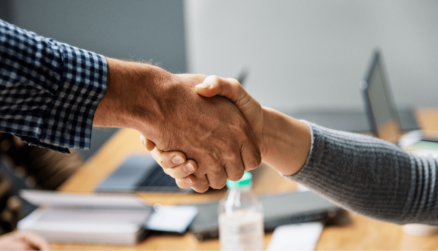 Business people shaking hands in agreement over a table of work supplies and laptops.