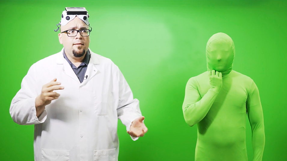 Man in white lab suit and goggles next to man in green bodysuit, both in front of green screen