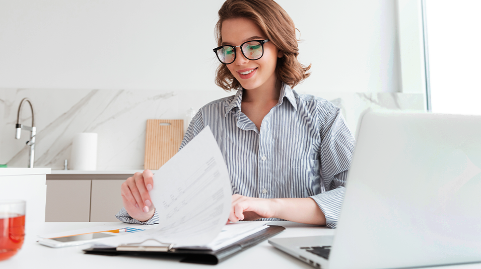 Smiling woman at desk, reviewing job applicant resumes.