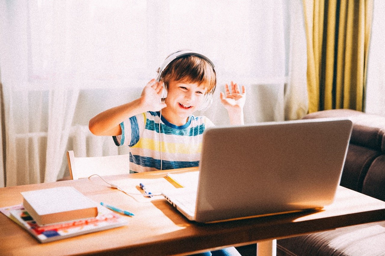 Early elementary-aged student wearing headphones and gesturing toward laptop for remote learning