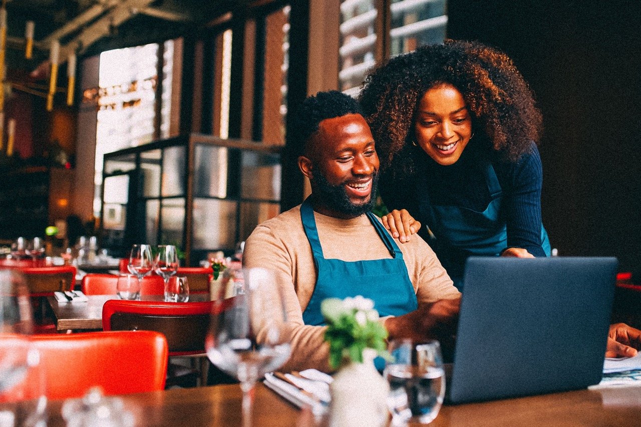 A man and woman, both small business owners, working together on a laptop in their restaurant.