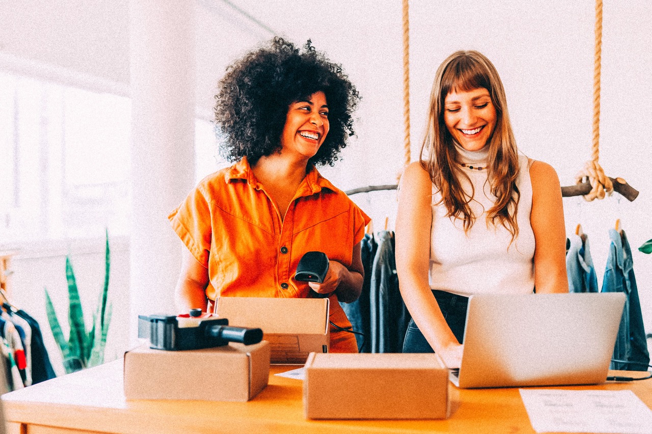 Two women small business owners packaging products and creating videos on a laptop