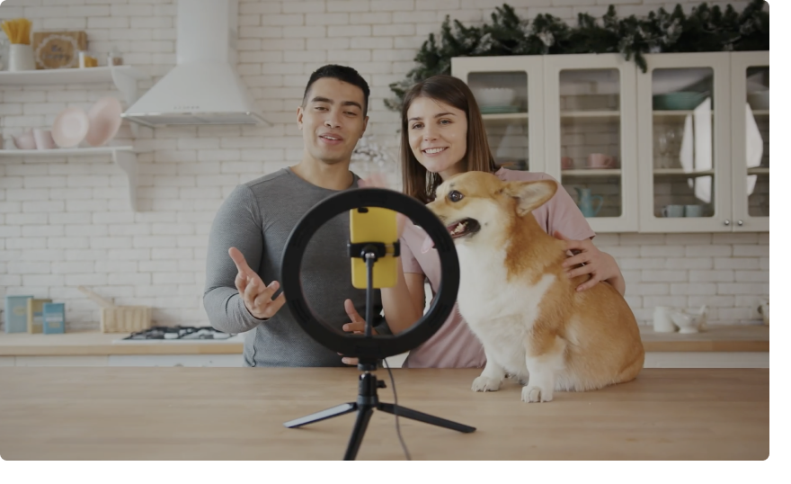A man and woman recording a video with their dog. 
